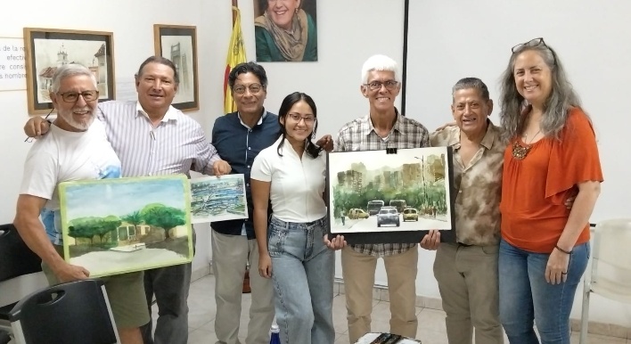 Grupo de seis personas sonriendo y sosteniendo pinturas en un espacio interior.